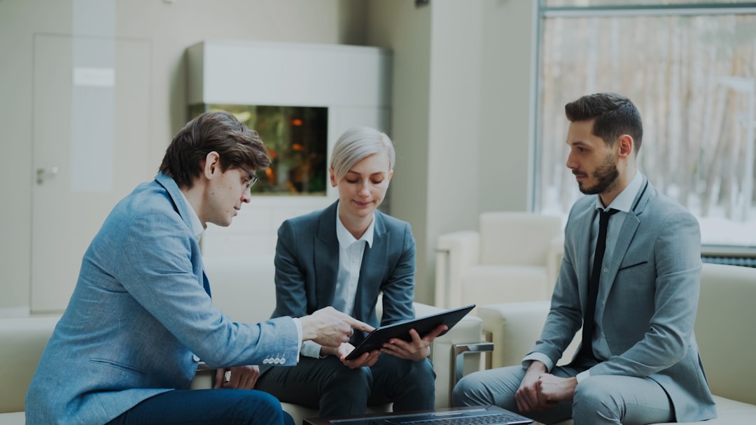 footer-cta-img Panning shot of businessman discussing financial reports with female and male business partners sitting on sofa in modern office hall with indoors